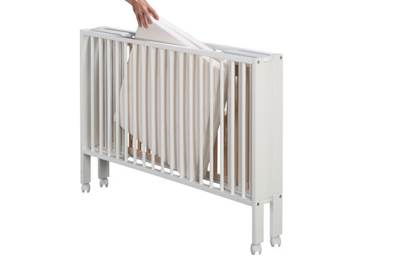 A person folding a white collapsible crib with wheels against a plain background.