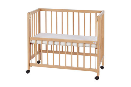 A wooden baby crib with slatted sides and wheels on a white background.