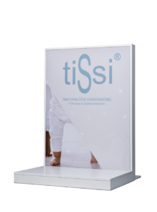 Sign displaying 'tiSsi' with a baby in patterned clothes standing on floor.