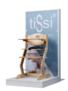 Wooden high chair on display stand against blue tiSsi branded backdrop.