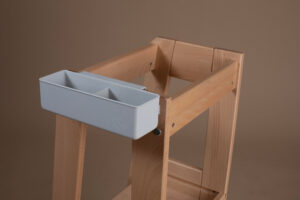 Wooden support structure with attached rectangular gray container on beige background.